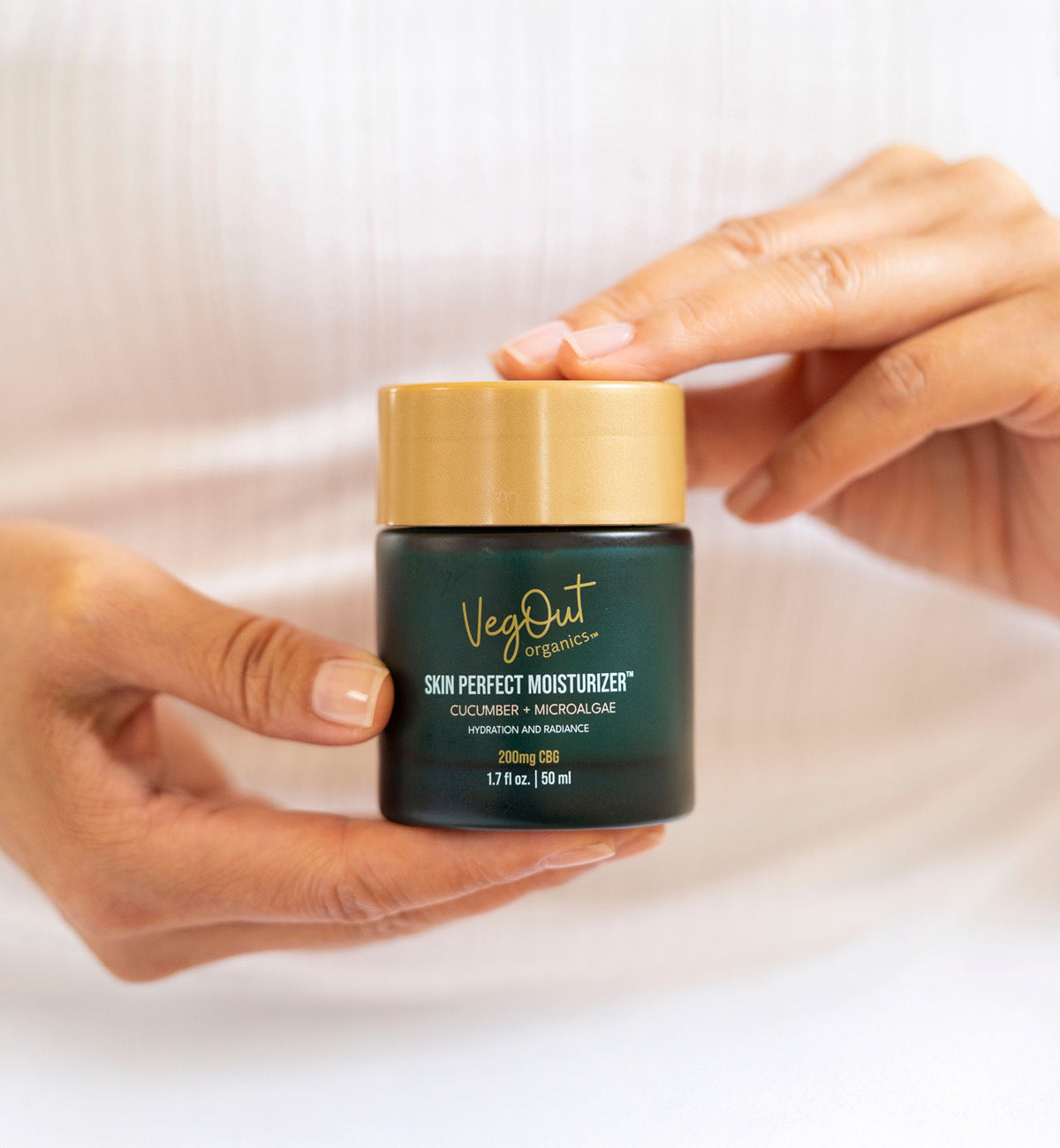 Close-up of a person holding a jar of VegOut Organics Skin Perfect Moisturizer, highlighting the product's label and elegant packaging.