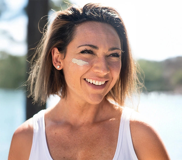 Mature woman smiling outdoors with clay face mask under her eye, promoting natural skincare and radiant aging with VegOut Organics