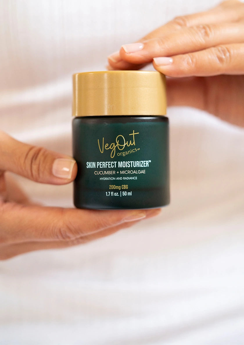 Hands holding VegOut Organics Skin Perfect Moisturizer with cucumber and microalgae for hydration and radiance.
