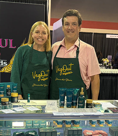 Brad and Katie Wynne, founders of VegOut Organics, standing at their trade show booth displaying their natural skincare product line.