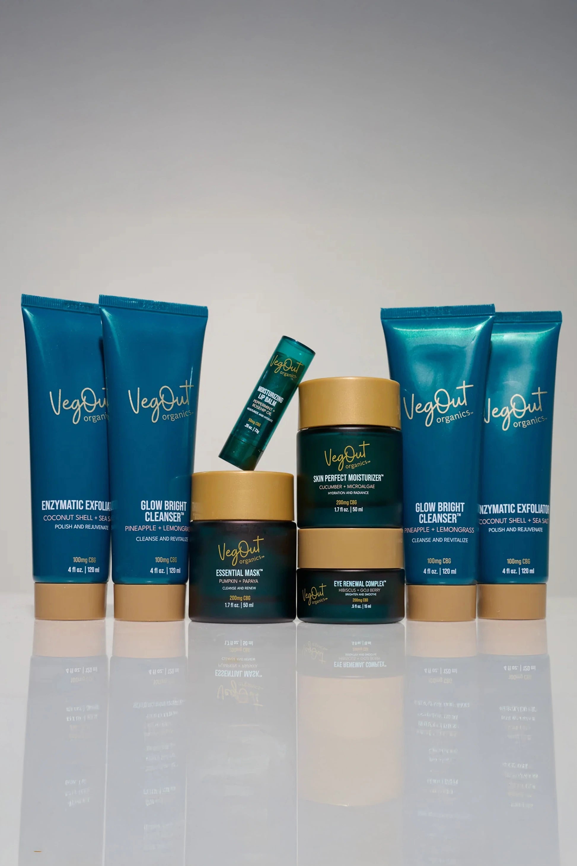 A complete set of VegOut Organics facial skincare products including Glow Bright Cleanser, Enzymatic Exfoliator, Essential Mask, Eye Renewal Complex, Skin Perfect Moisturizer, and Lip Balm, beautifully arranged against a neutral background. This Facial Deluxe Bundle offers a plant-based, non-toxic skincare routine enriched with Aloe Vera, Papaya Enzymes, and Hemp Extract for glowing, healthy skin.