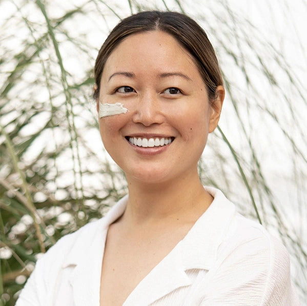 Smiling woman applying Veg Out Organics vegan face clay mask with plant-based ingredients.